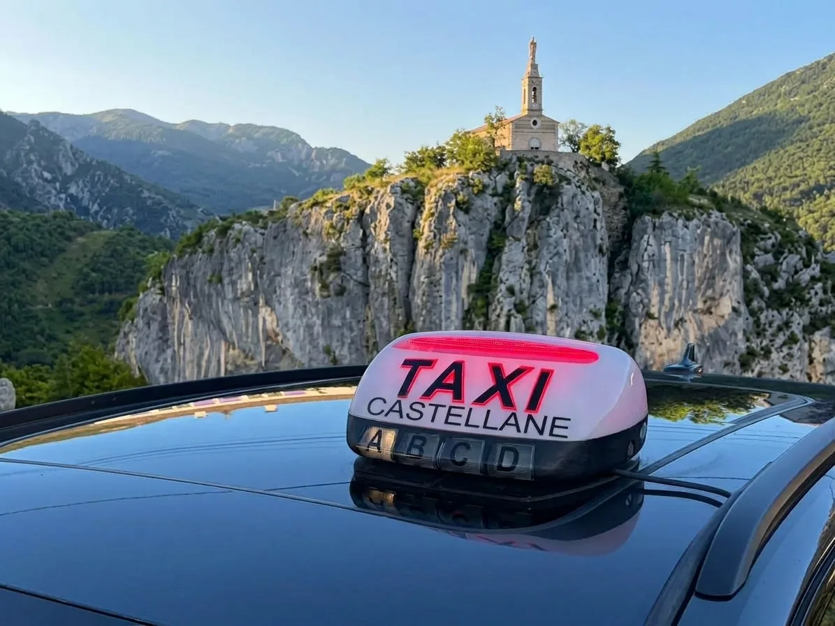 Enseigne TAXI CASTELLANE sur le toit d’un taxi, devant le rocher et la chapelle Notre-Dame du Roc